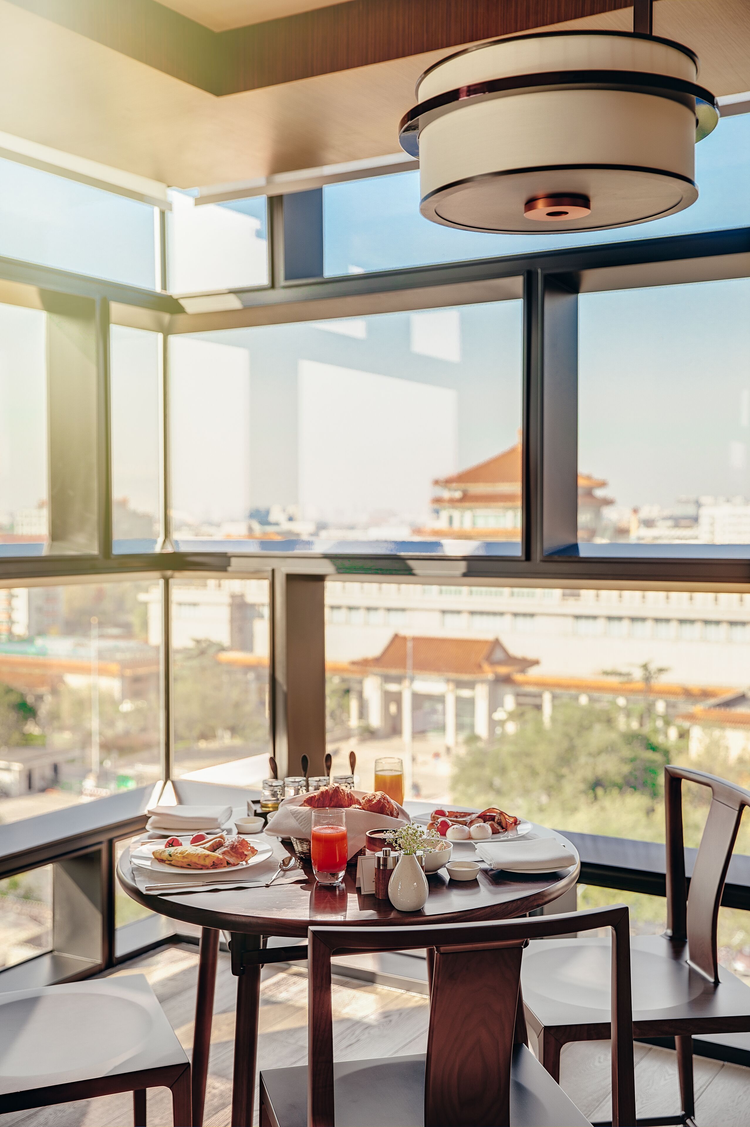 A dining table with breakfast items and a city view through large windows.