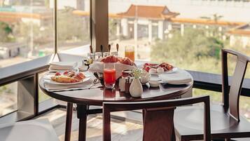A dining table with breakfast items and a city view through large windows.