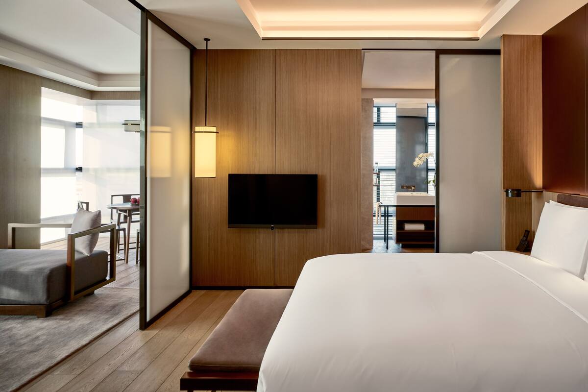 A modern hotel room with a large bed, a flat-screen TV, a desk with a chair, and a bathroom visible through an open door.