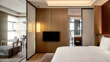 Habitación de hotel moderna con una cama grande, televisión de pantalla plana, escritorio con silla y baño a la vista a través de una puerta abierta.