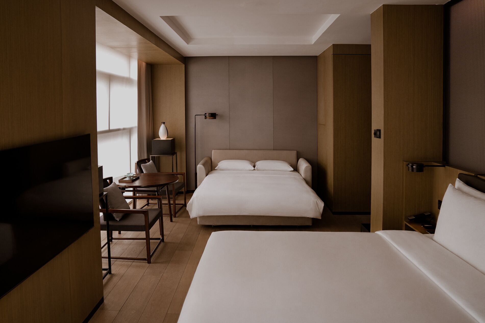 A hotel room with a bed, a desk, a chair, a lamp, and a television.