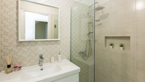 A bathroom with a glass-enclosed shower, a sink with a mirror above it, and two small potted plants on the wall.