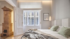 A bedroom with a large bed, a wooden cabinet, and a window with a view of buildings.