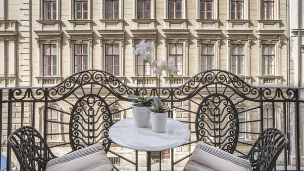 A balcony with a round table, two potted plants, and a wrought iron railing.