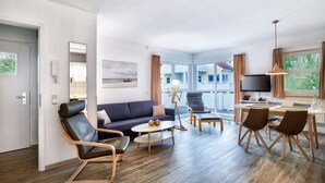 Una habitación de hotel moderna con sofá, sillas, una mesa de comedor y televisión.