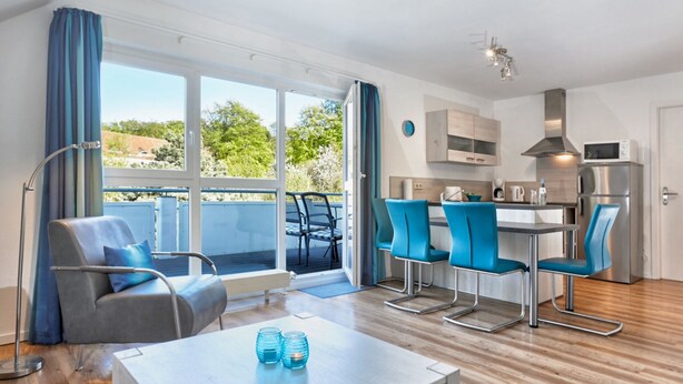 Una sala de estar moderna con un sofá y sillones, un comedor con una mesa y una cocina equipada.