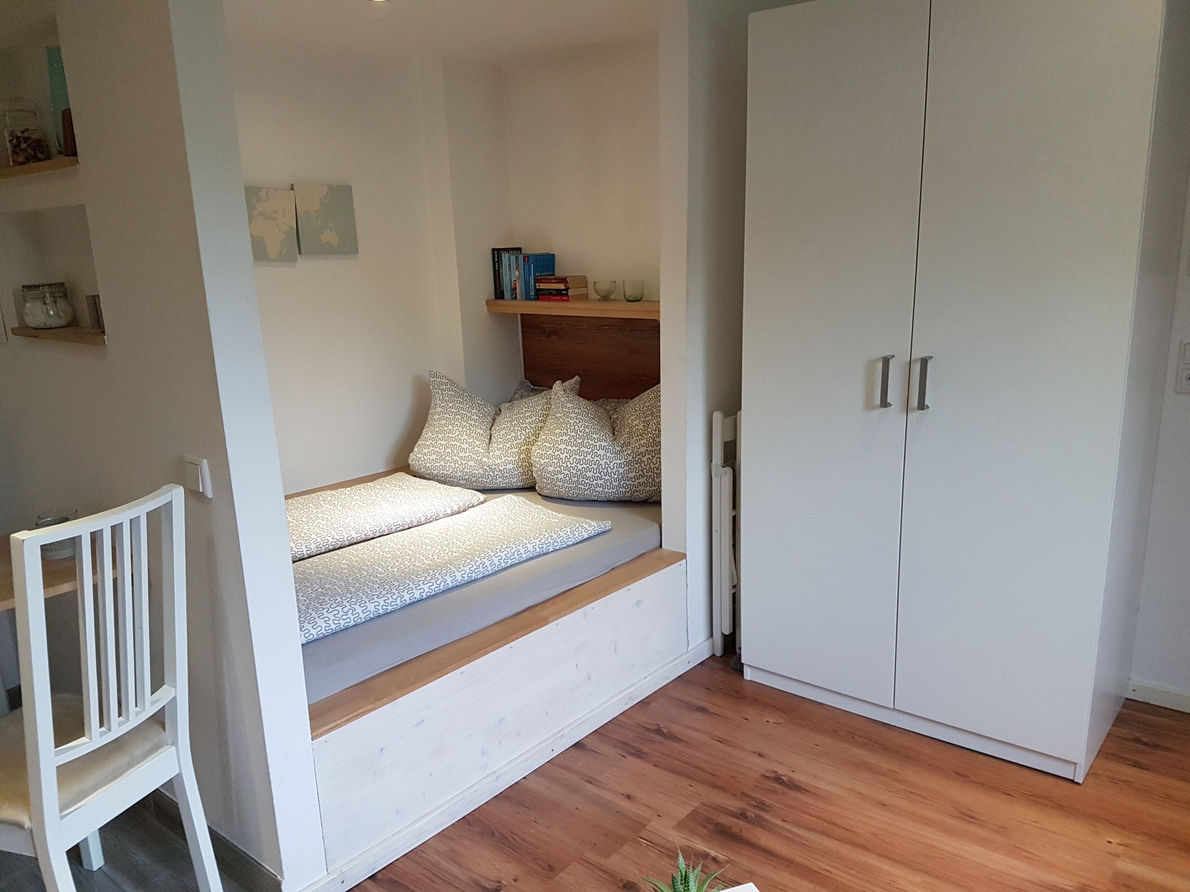 A bedroom with a built-in bed, a wardrobe, and a small shelf with books.