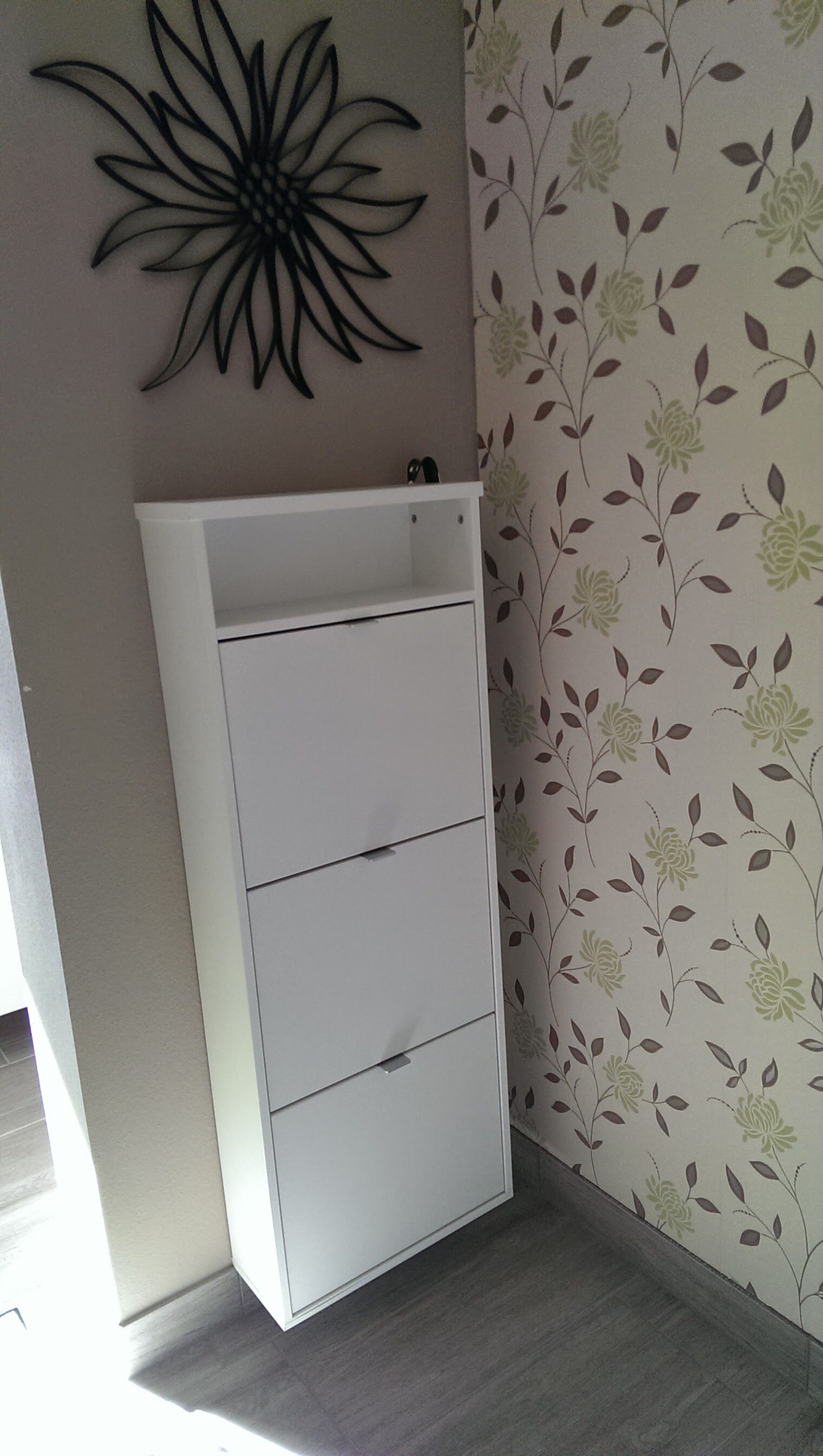 Un archivador blanco en una habitación con papel tapiz floral y una obra de arte abstracta negra en la pared.
