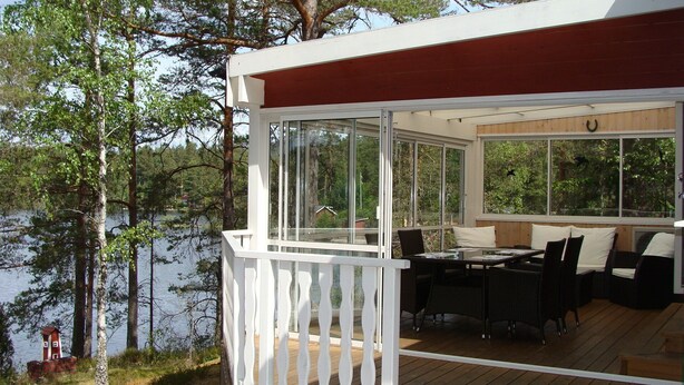 Terraza techada al aire libre con una mesa y sillas, con vista a un lago.