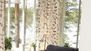 Una sala de estar acogedora con un sofá gris, una mesa de centro de madera y vistas a árboles a través de amplias ventanas.