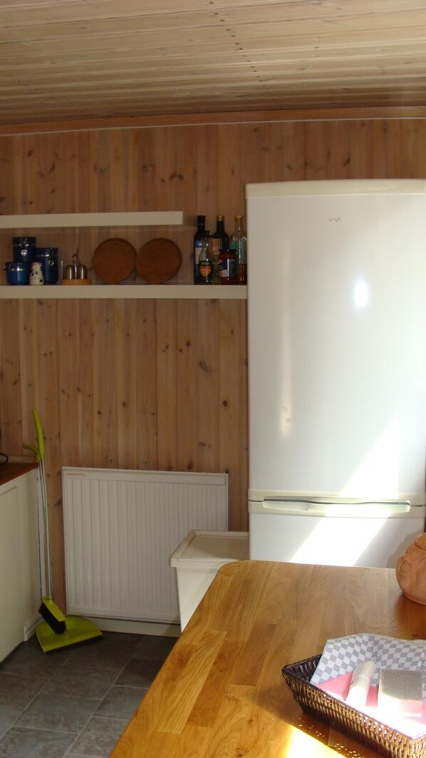 Ett kök med träväggar, ett vitt kylskåp, ett träbord och en sopkvast.