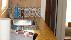Cocina con paredes de madera, un lavamanos, un reloj y una puerta que da a otra habitación.