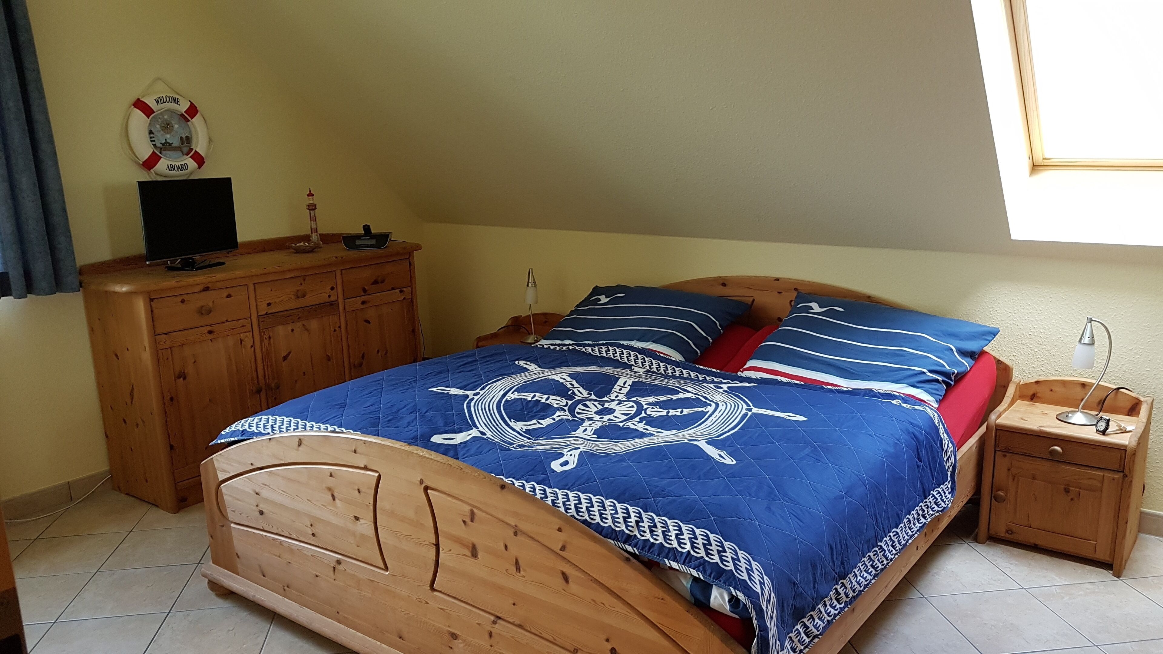 Ein Schlafzimmer mit einem hölzernen Bett, einer Holzkommode, einem Nachttisch mit Lampe und einer Wanduhr.