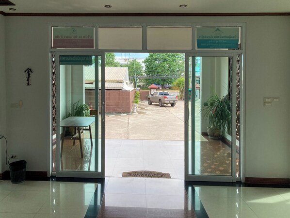 A hotel entrance with a glass door, a reception desk, and a view of the parking area. - Rueanchorfa Hotel (Nongbua Lamphu)