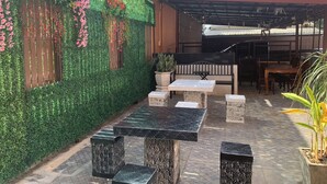 Een terras buiten, met een groene wand, zitgedeelte en tafels.
