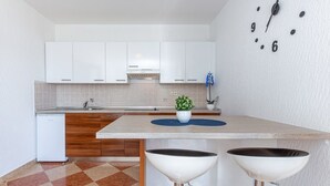 A modern kitchen with white cabinets, a central island, two bar stools, a clock on the wall, and a small potted plant.