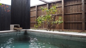 A clear pool with a wooden deck, a stone bench, and a small tree. - Yufuin Rikka (Yufu)