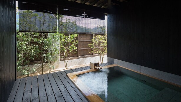 A traditional Japanese onsen with a wooden deck, a hot spring bath, and a view of bamboo and mountains. - Yufuin Rikka (Yufu)