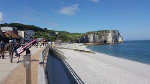 A coastal promenade with a pebble beach, a promenade with a railing, and white cliffs in the background. -  Quiet 3* Cottage 10m from Étretat | Fenced Garden | Dogs Welcome  Farm animals (Criquetot L Esneval)