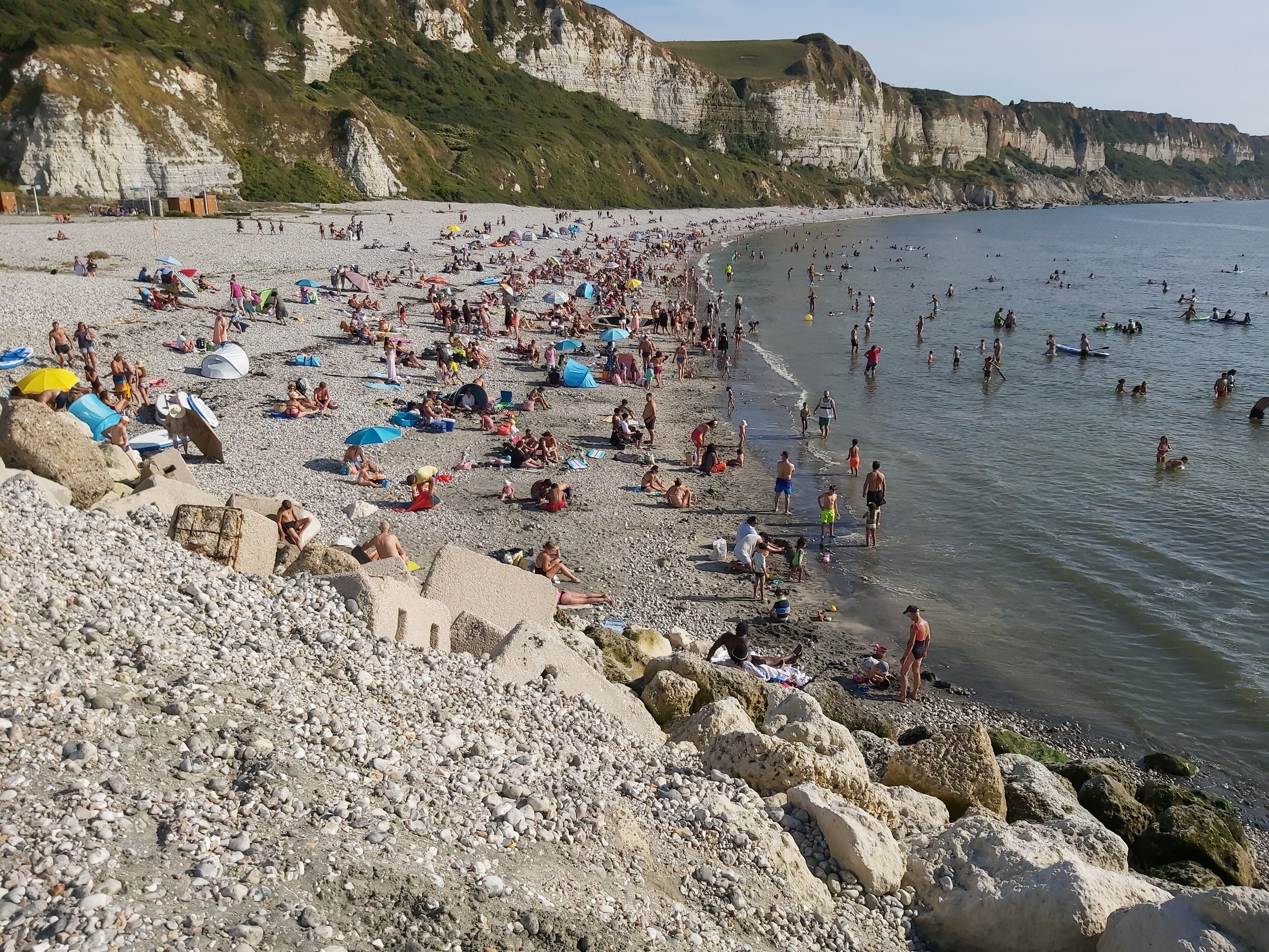 Een druk strand met mensen die zonnebaden en zwemmen.