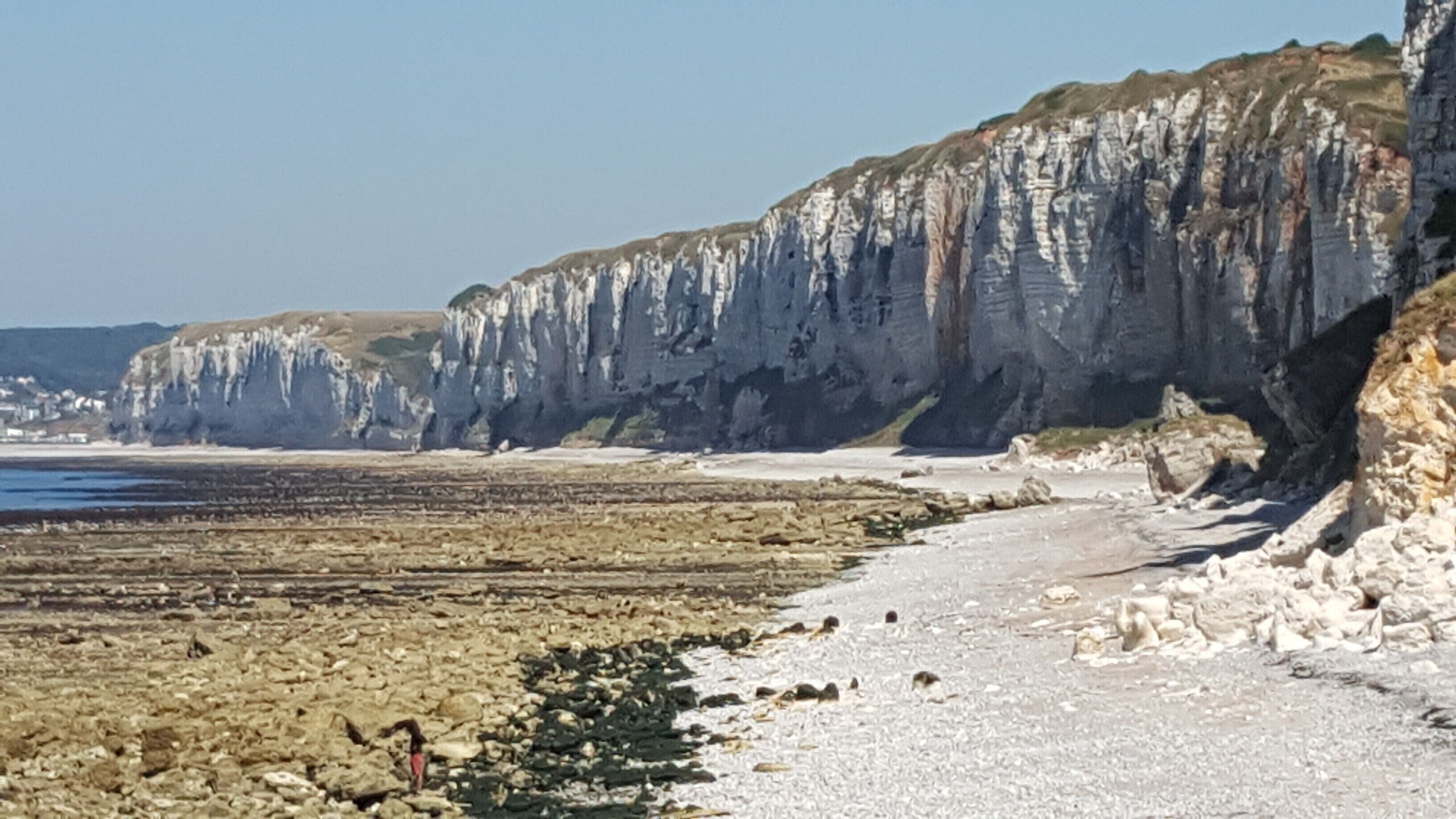 A coastal landscape with white cliffs, a pebble beach, and a calm sea.