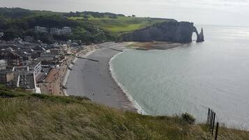 Une ville côtière dotée d’une longue plage de sable, d’une falaise percée d’une arche naturelle et de bâtiments qui bordent le rivage.