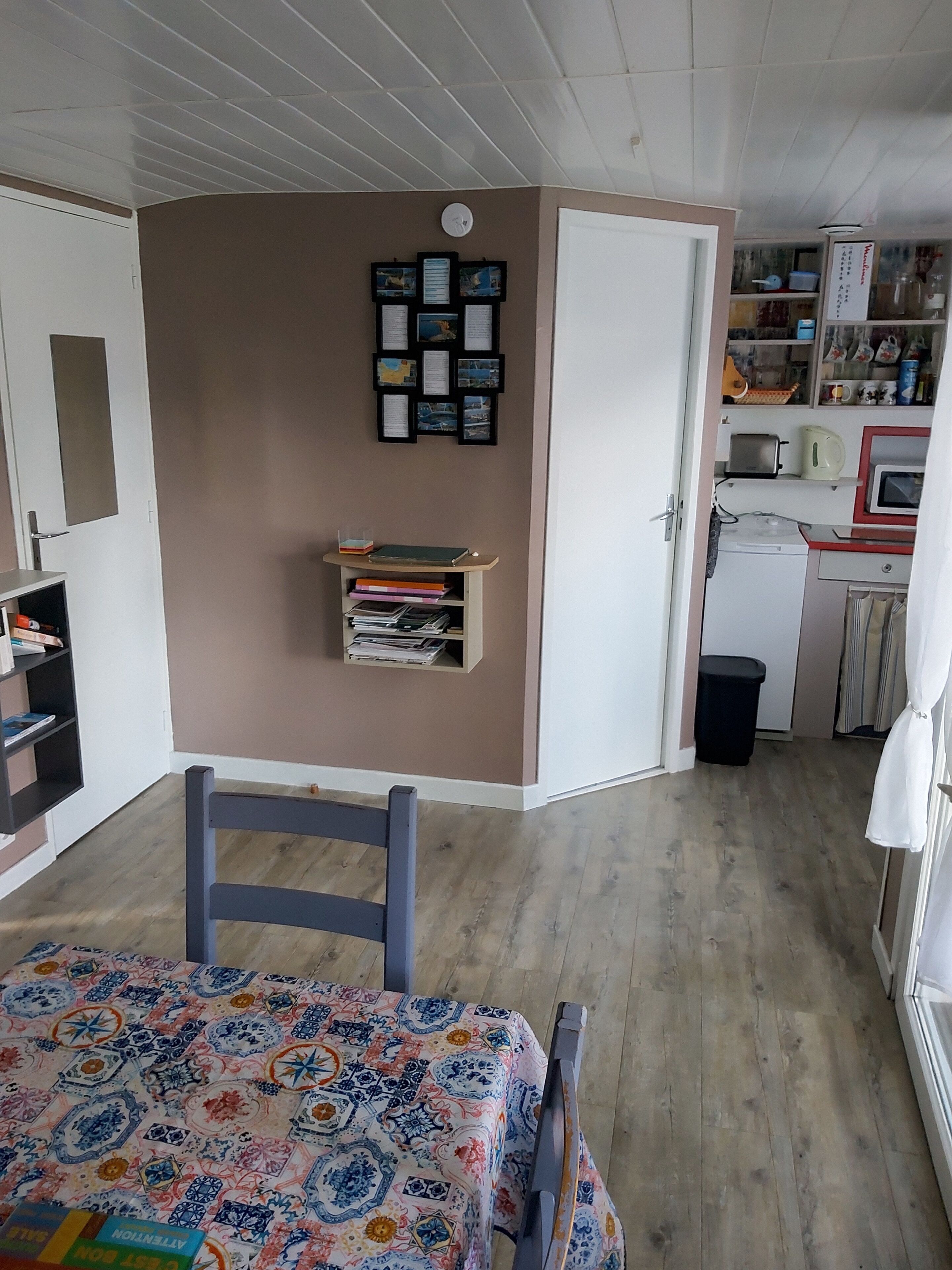 Een kleine kamer met een bed, een klein bureau, een kitchenette en een wandplank met ingekaderde foto’s.