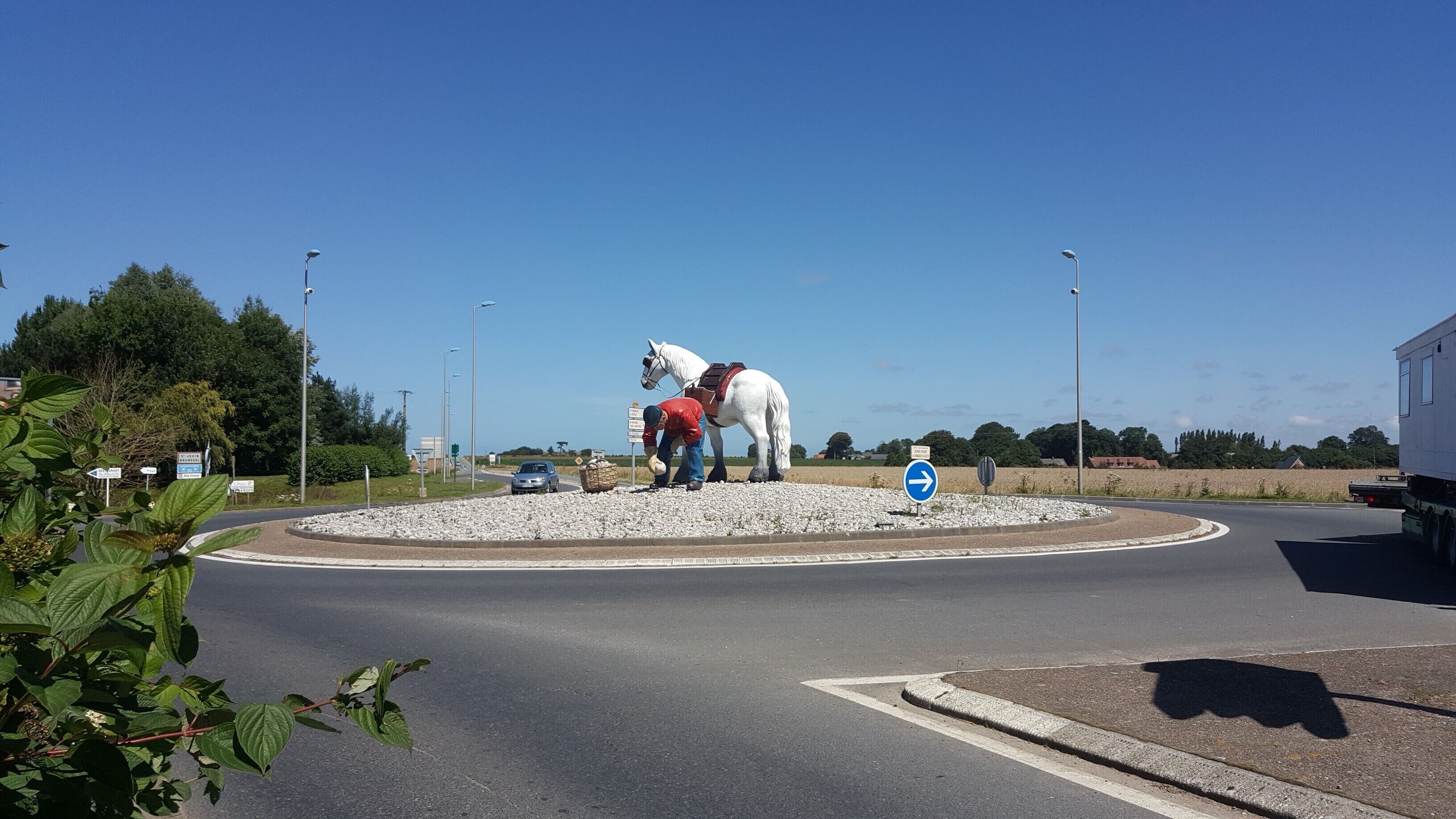 Un rond-point orné d’une statue de cheval blanc, avec un homme portant une veste rouge et un panneau de signalisation bleu.