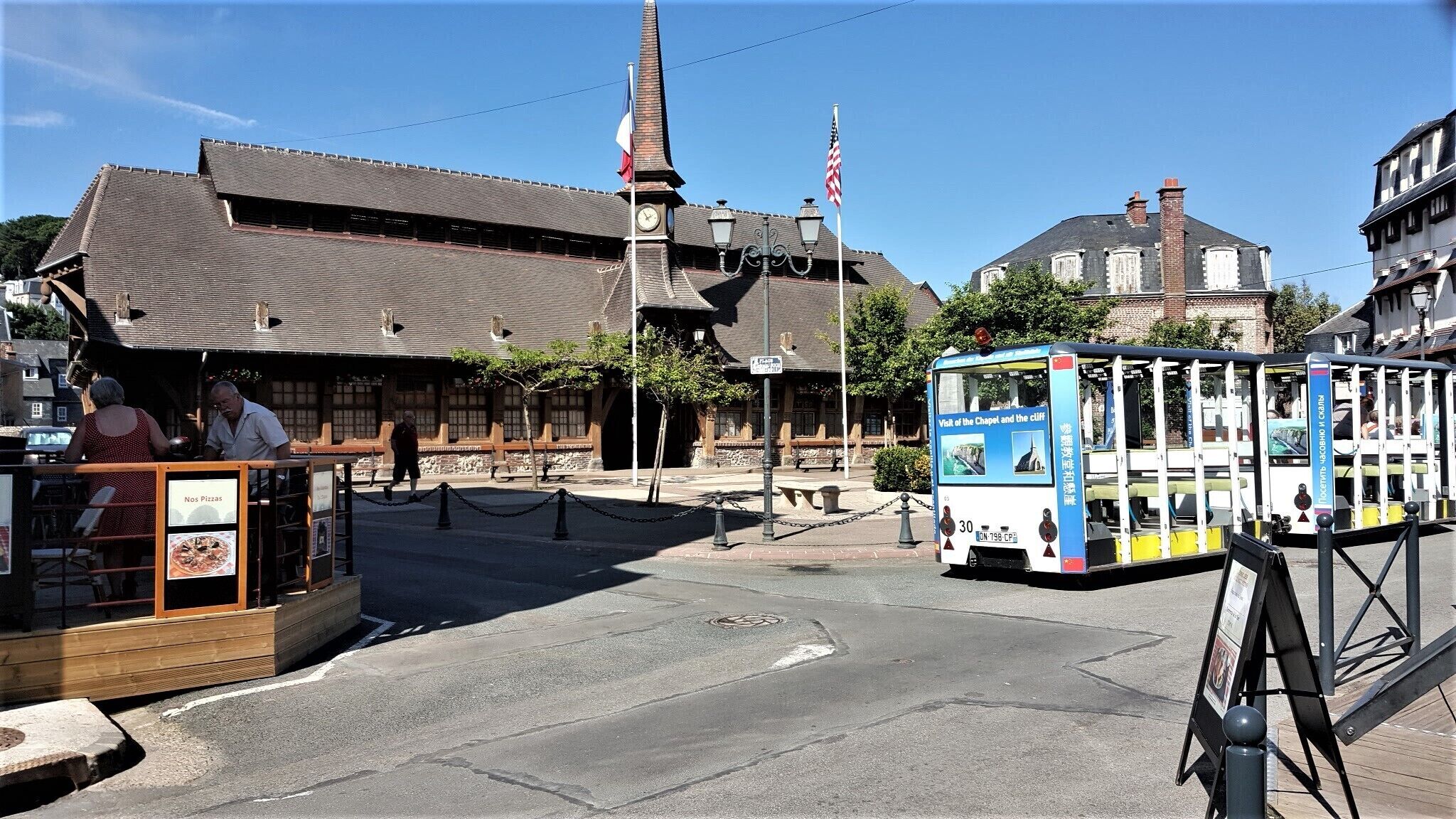 A historic building with a clock tower, a tram, and a sign for 'Nos Pizzas.'