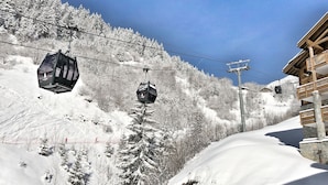 A ski lift with cabins, a wooden building with balconies, and a snowy mountain slope.