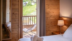 A wooden room with a bed, a nightstand with a lamp, and a balcony with a chair.