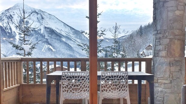 A wooden deck with a table and chairs, overlooking a snowy mountain landscape.