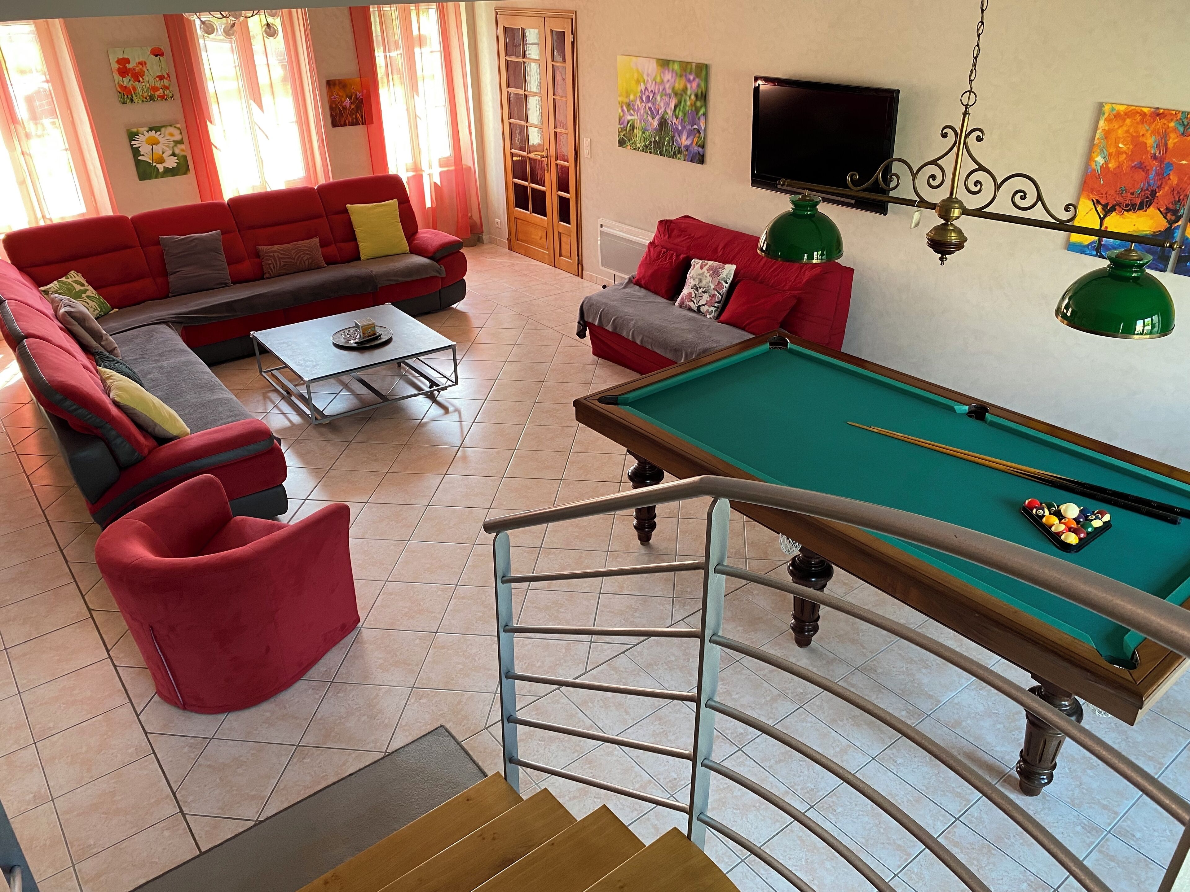 A living room with a pool table, red sofas, a TV, and artwork on the walls.