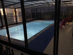 Una piscina interior con cerramiento de vidrio, rodeada por un suelo estampado y algunas sillas.