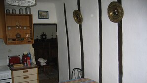 Een kleine, gezellige kamer met een gestreept beddegoed, een houten kast met keukengerei, een fornuis en een stoel.