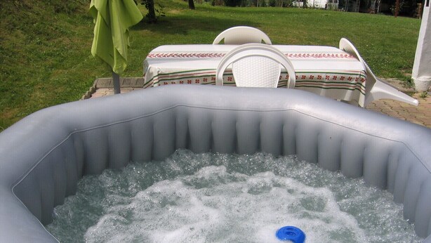 Een opblaasbaar bubbelbad met een blauwe uitloop, omringd door gras en een tafel met stoelen.