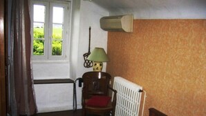 Een slaapkamer met een houten bed, een stoel met een rode kussen, een radiator en een raam met gordijnen.