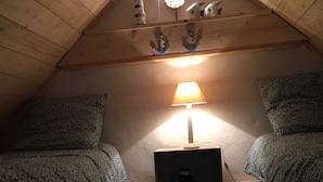Um quarto de sótão acolhedor com duas camas, uma lâmpada e objetos decorativos no teto inclinado.