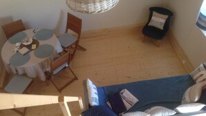 Um quarto pequeno e acolhedor com uma mesa redonda, duas cadeiras de madeira, um sofá azul com almofadas e um candeeiro pendente de vime.