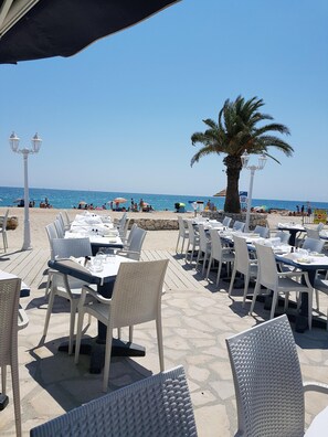 Un espace de restauration en plein air avec des tables et des chaises, un palmier et une vue sur la plage et l’océan.