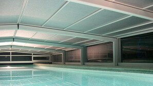 A modern indoor swimming pool with a clear water surface, surrounded by walls with large windows and a ceiling with a grid pattern.