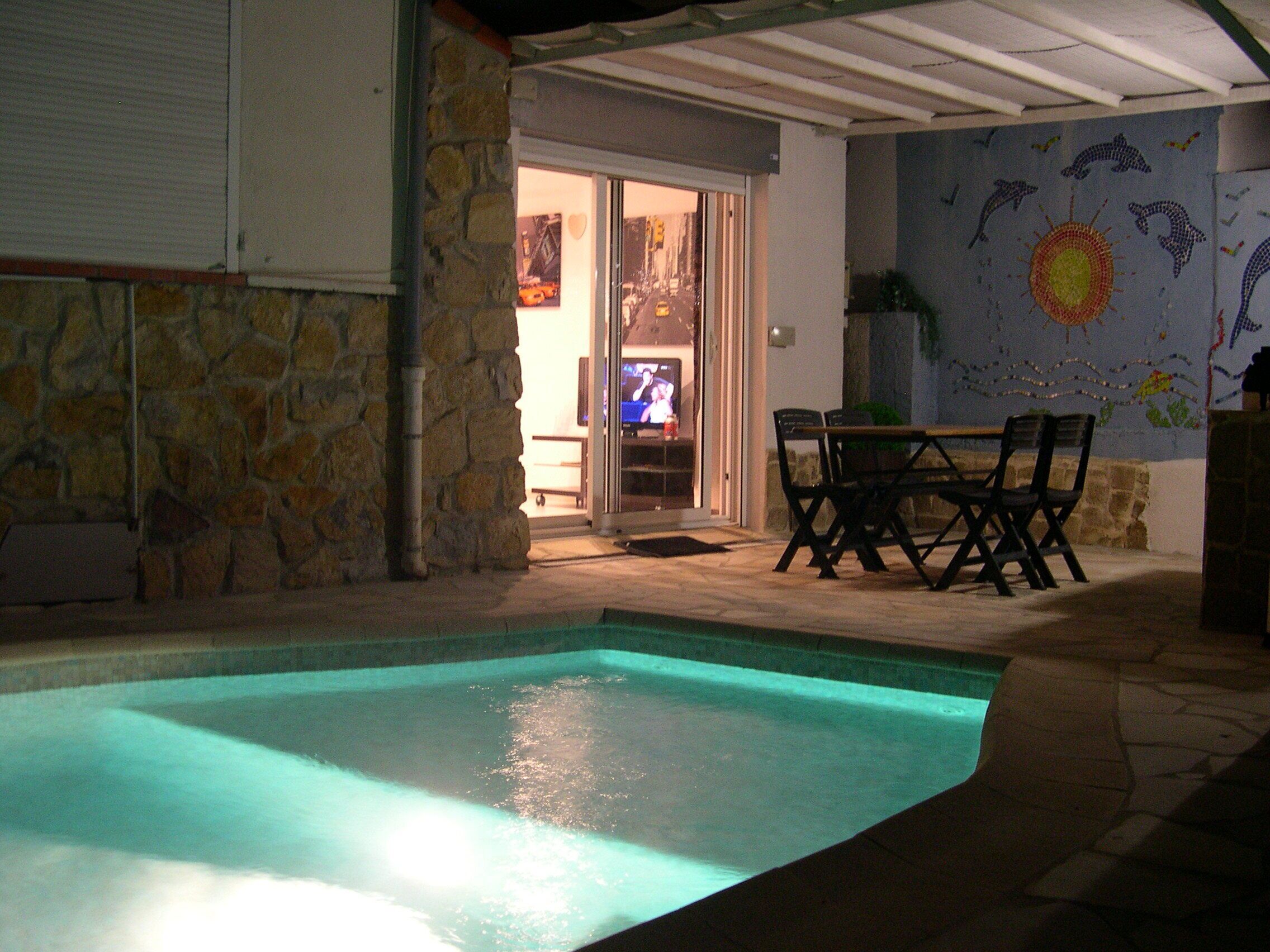 An outdoor swimming pool area with stone walls, a patio table, and chairs.