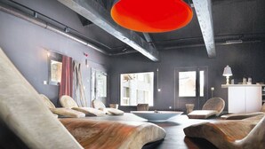 Ein moderner Wellnessraum mit Holzstühlen, einer zentralen Wassereinrichtung und einem großen Fenster, das für natürliches Licht sorgt.