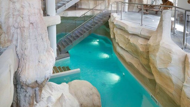 Ein Hallenbad mit Felslandschaft und einer Treppe, die zu einer erhöhten Ebene führt.