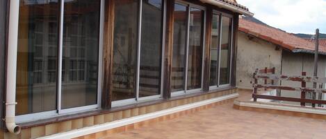A building with large windows, a tiled patio, and a balcony with a railing.