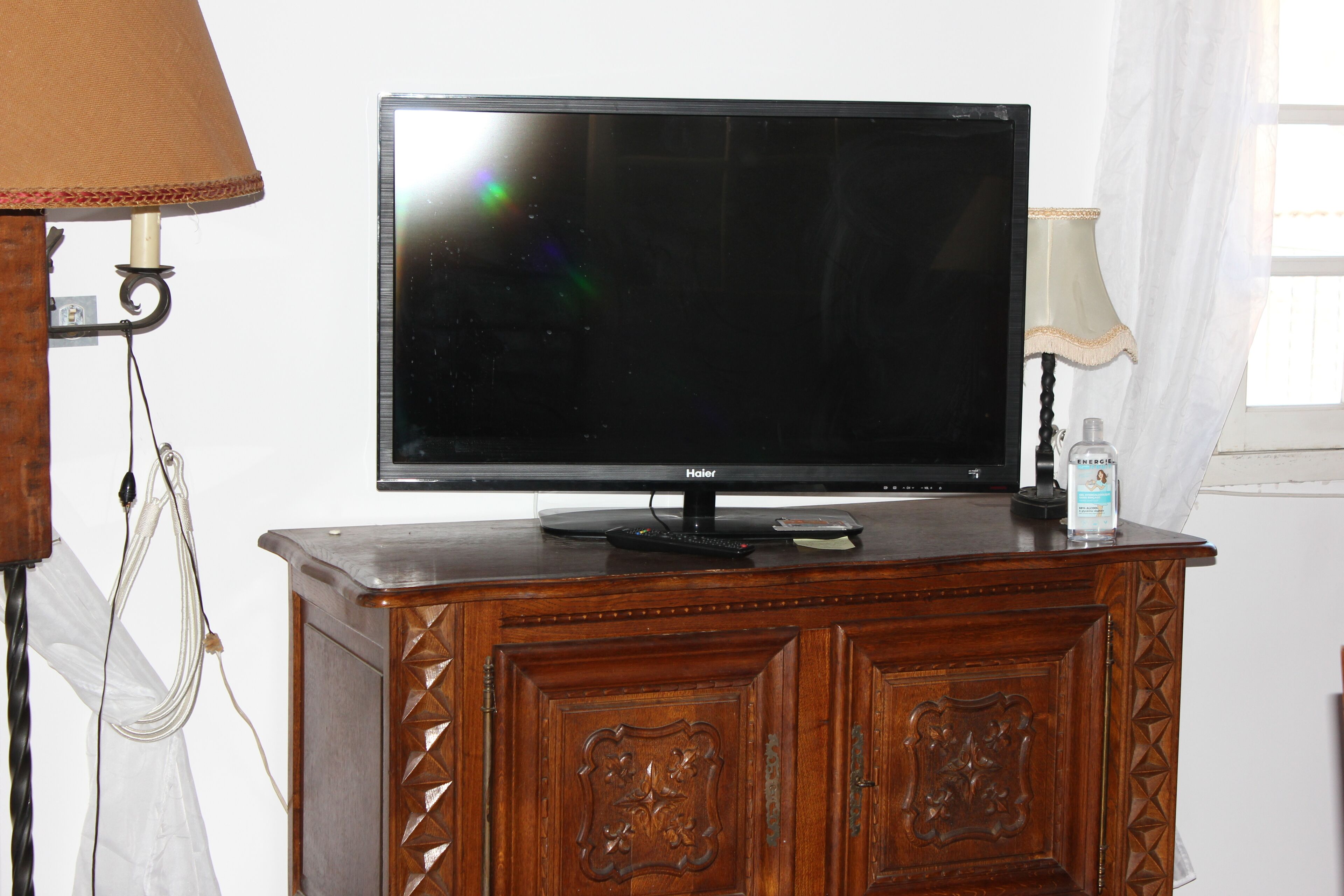 A flat-screen TV on a wooden cabinet with a lamp to the left.