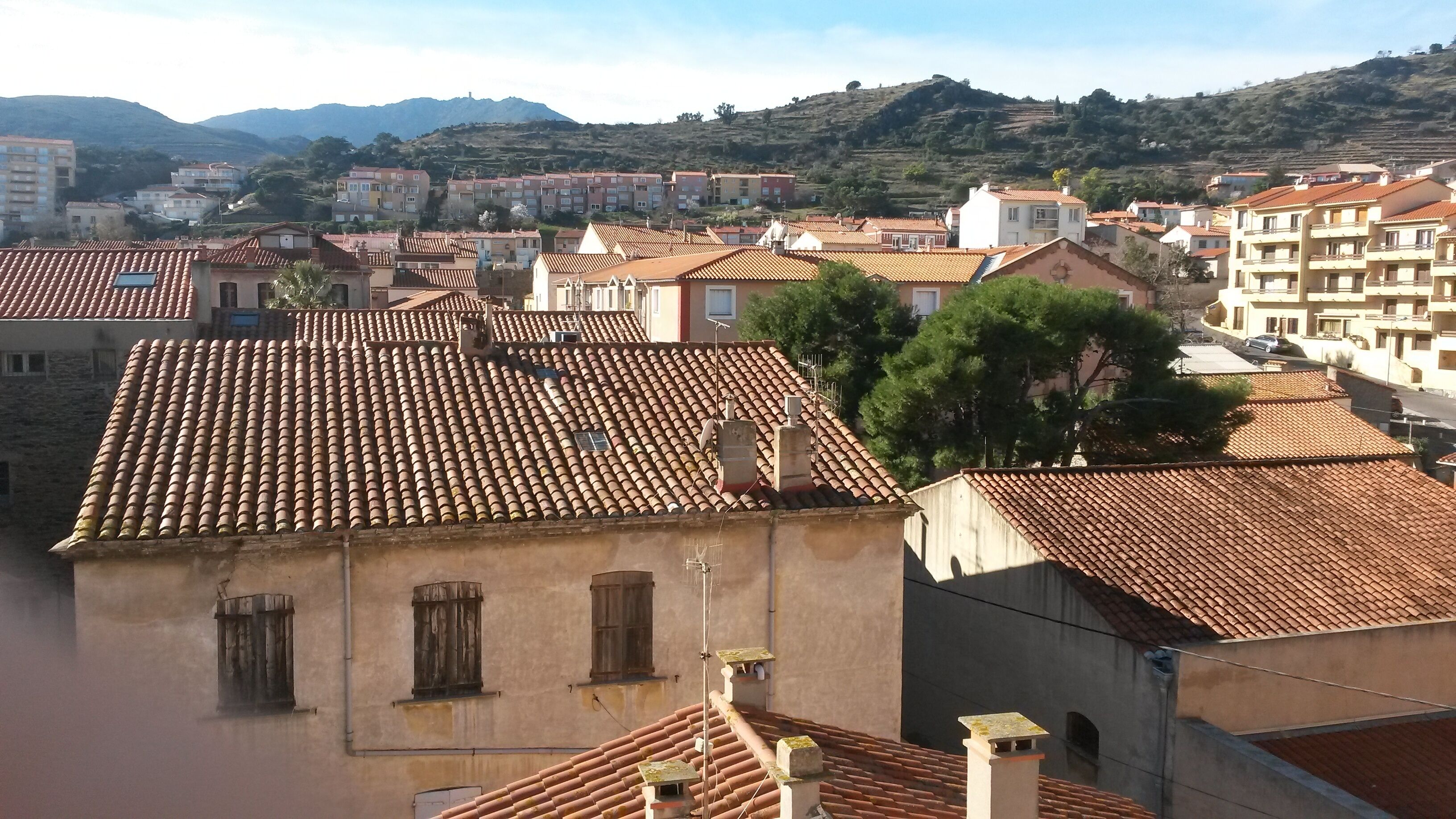 A residential area with terracotta-tiled roofs, a mix of single and multi-story buildings, and a hilly backdrop.