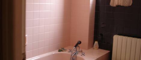 A bathroom with a pink tiled wall, a bathtub, a small white chair, and a window with a curtain.