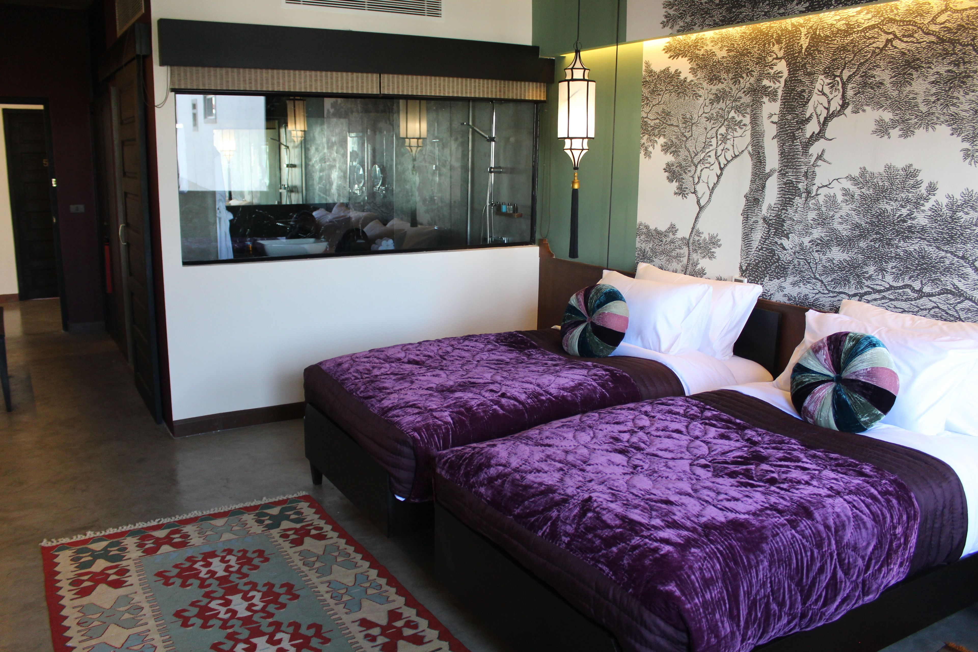 A hotel room with two beds, a large mirror, a wall mural, and a patterned rug.