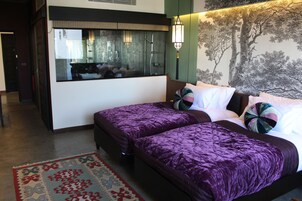 A hotel room with two beds, a large mirror, a wall mural, and a patterned rug.